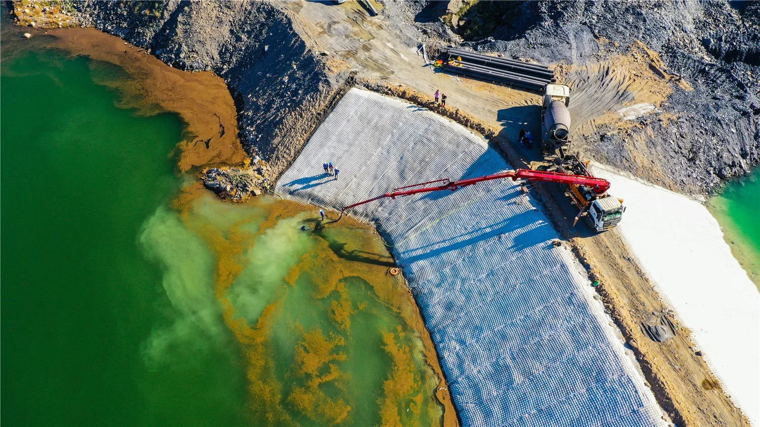 Aerial view showing grouted mattress installation on reservoir embankment upstream slope with pump trucks