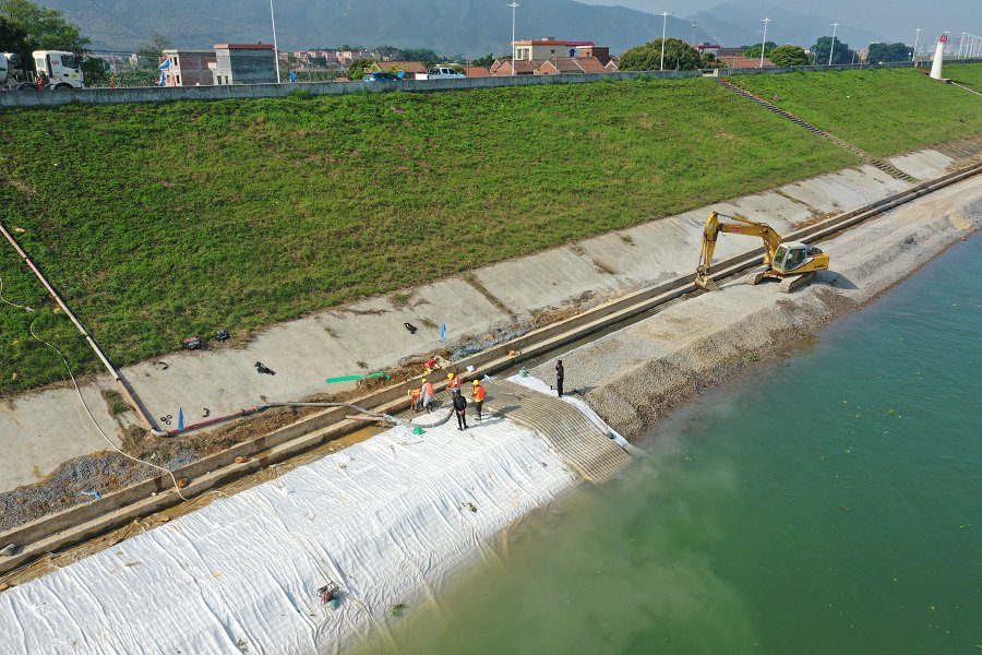 Installation crew with excavator laying grouted mattress on river bank