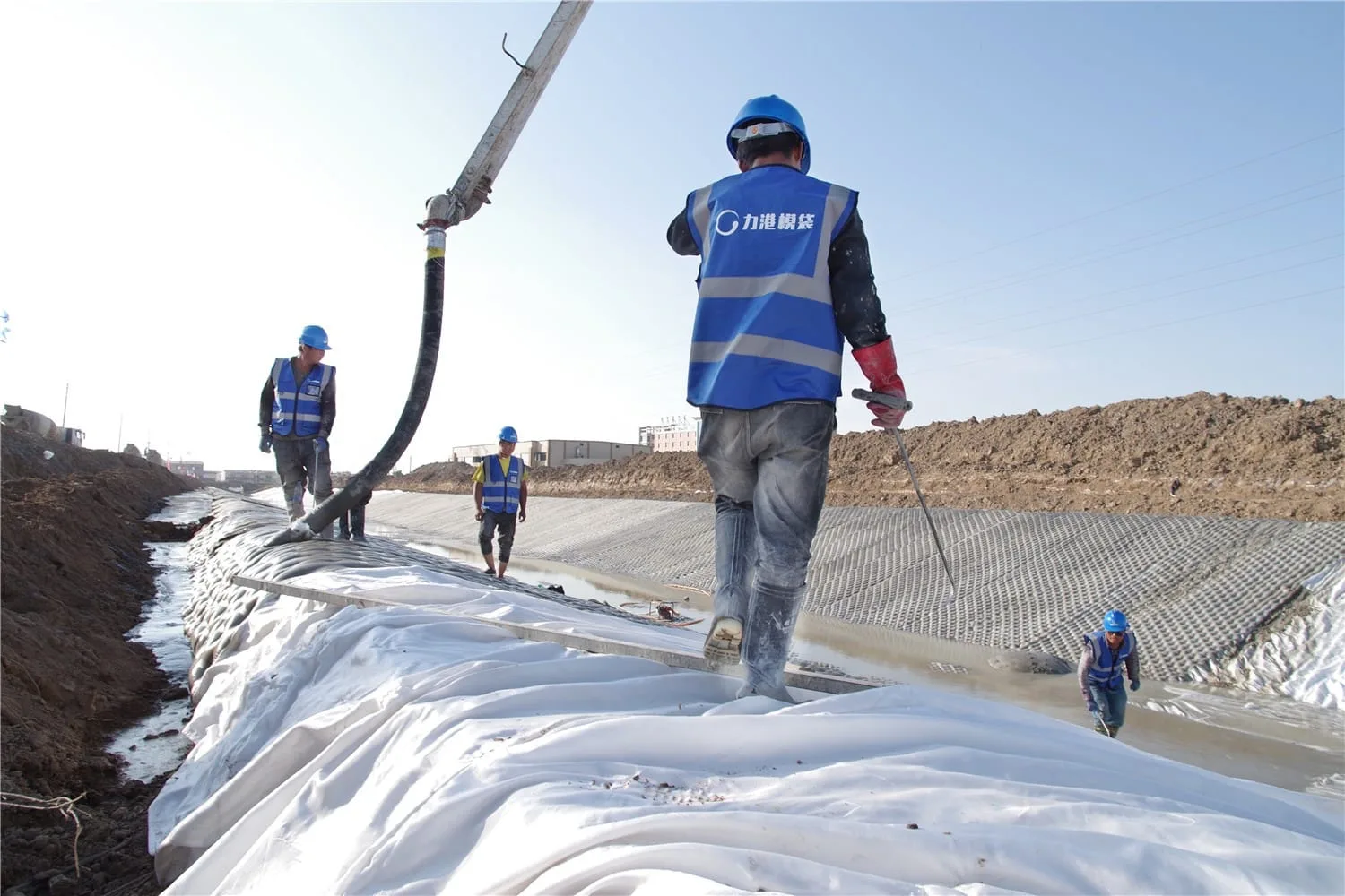 Workers injecting cement grout into articulated concrete mattress cells during canal lining installation