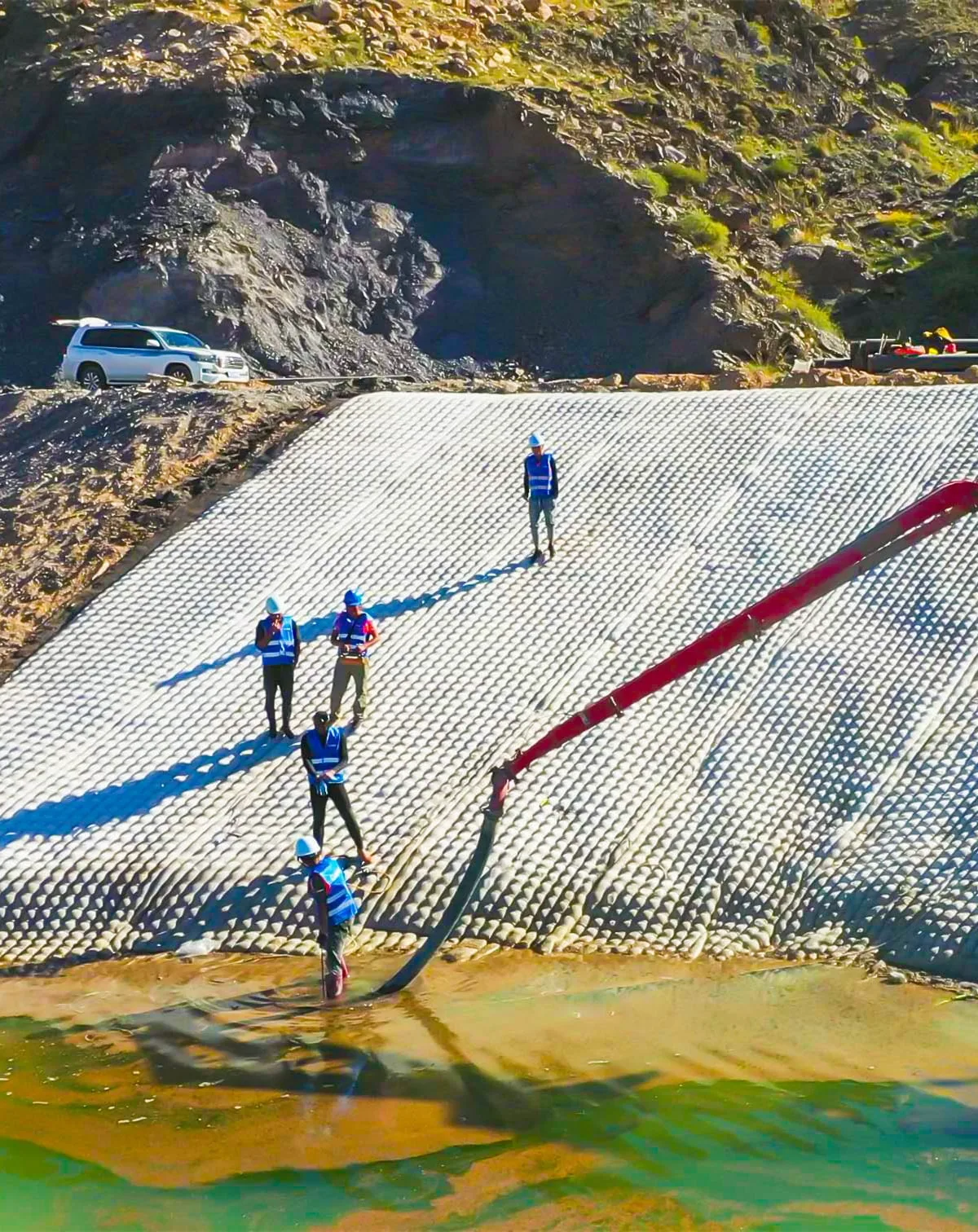 Workers and pump equipment at grouted mattress installation on reservoir embankment showing quality installation procedure